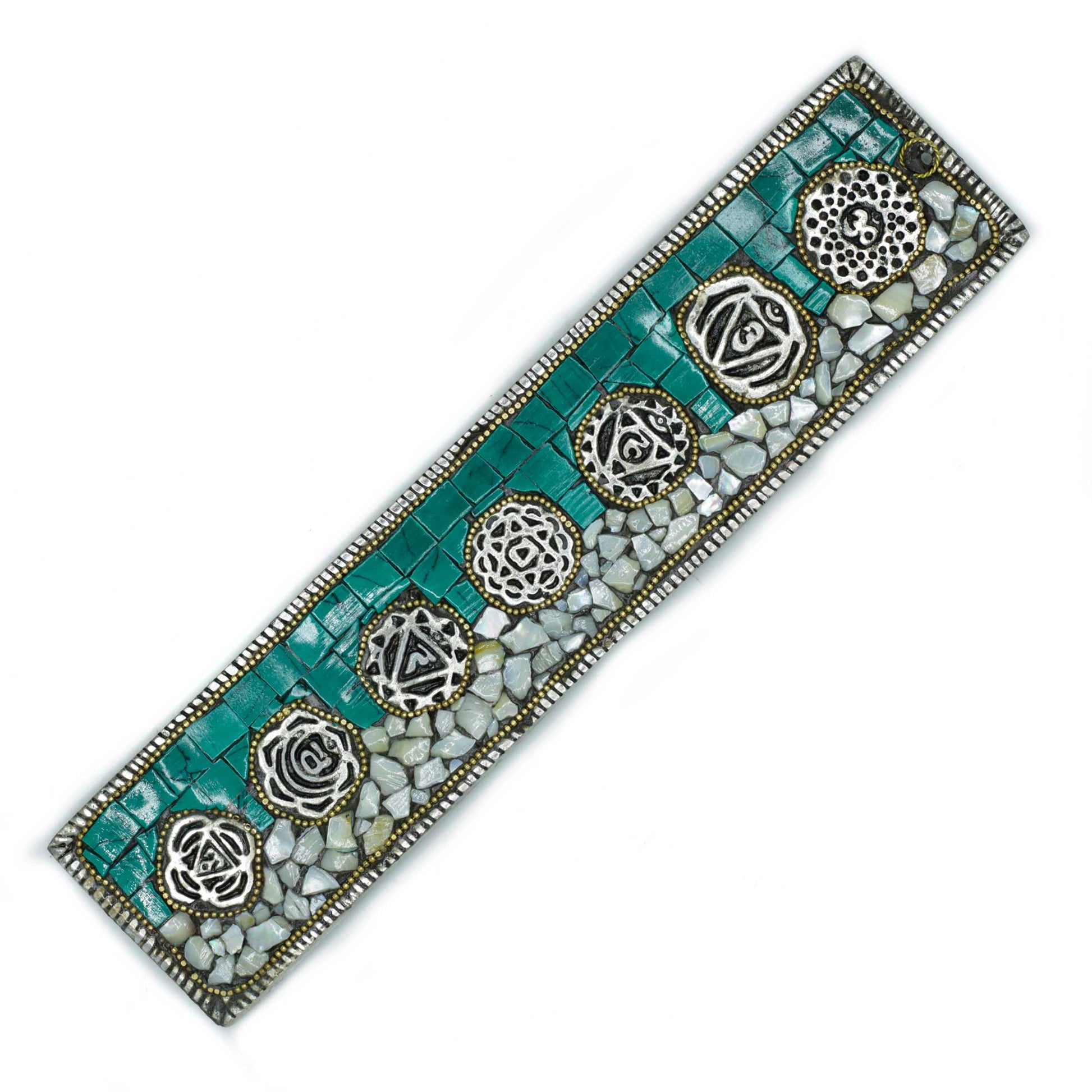 A rectangular mosaic bookmark displays intricate circular symbols embedded in teal and white stone tiles, bordered by tiny metallic beads, creating an ornamental, artistic design.