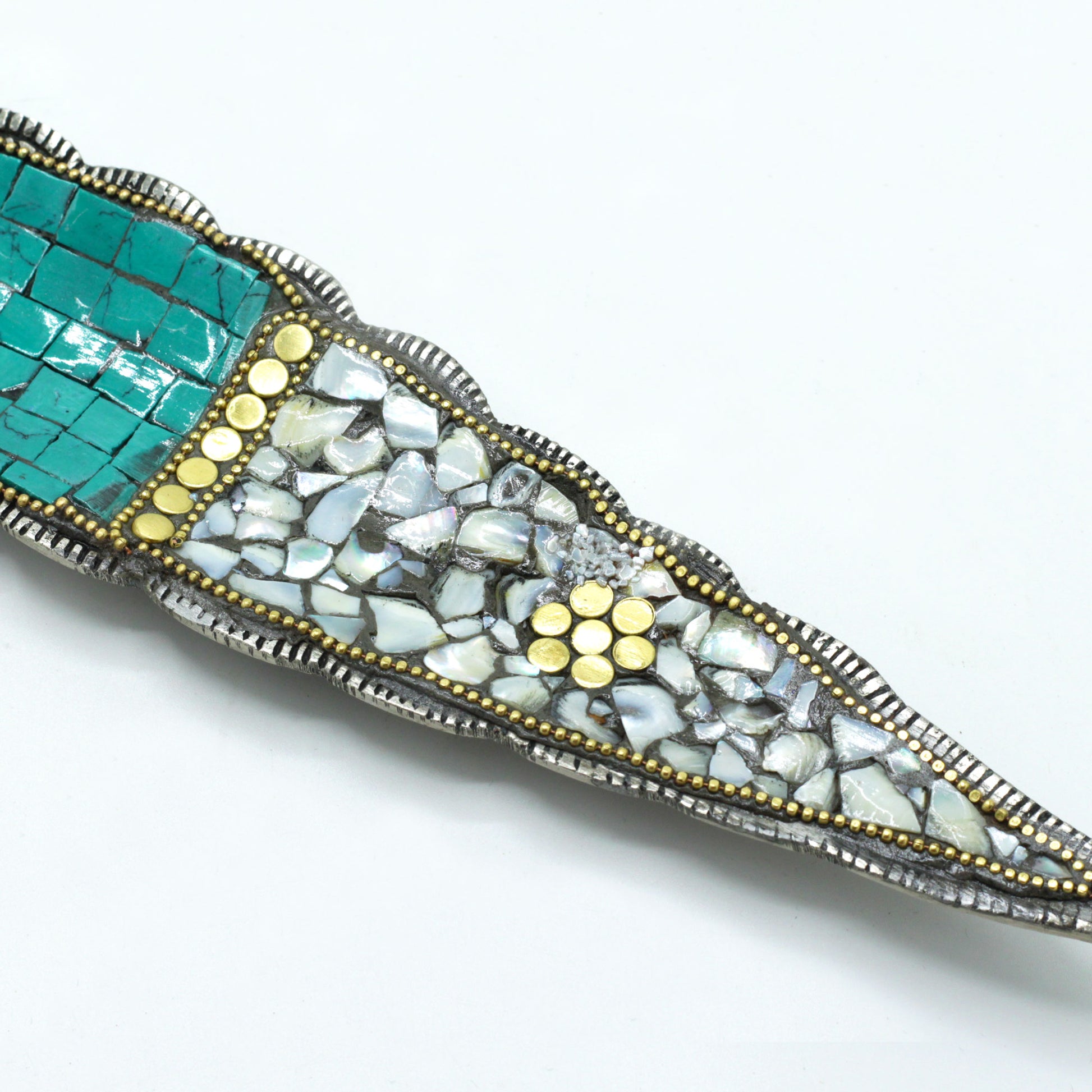Decorative knife handle adorned with turquoise mosaic tiles and mother-of-pearl pieces, accented by small yellow circular patterns, on a white background.