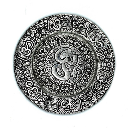 A circular decorative plate displays intricate patterns and the "Om" symbol engraved at the center, surrounded by ornate designs. The plate has a metallic appearance against a plain background.