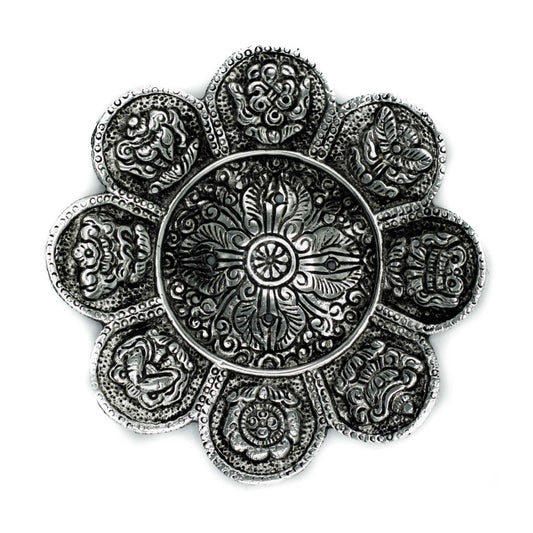Intricately designed silver plate features a central floral pattern. Surrounding motifs form a circular, petal-like arrangement with detailed textures, set against a plain white background.