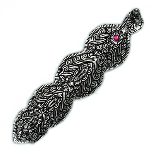 An intricately designed silver metal object resembling a feather, featuring swirling patterns and a central pink gem. The object is set against a plain white background.