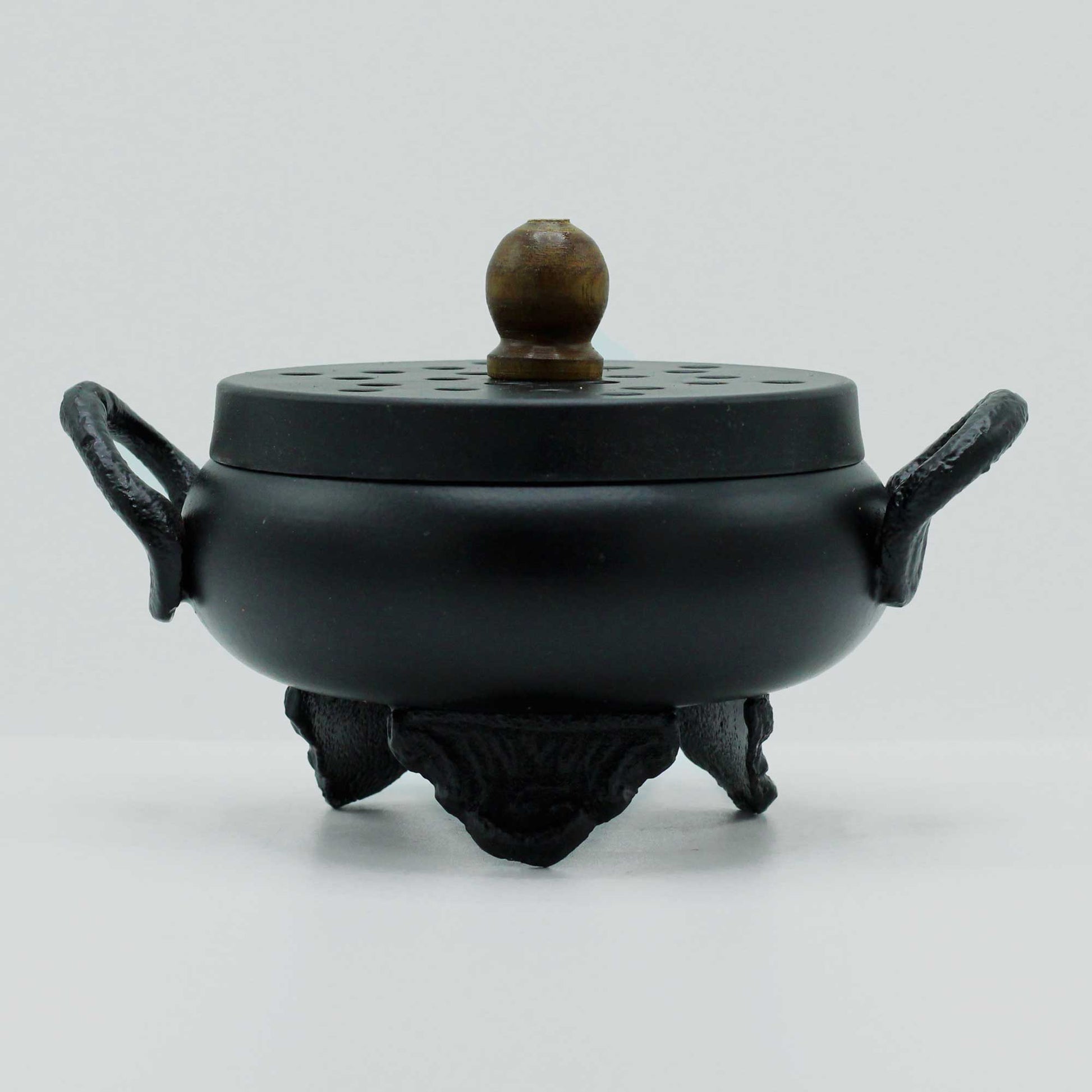 Black incense burner with a round body and lid featuring a wooden knob on top, resting on three ornate legs, against a plain white background.
