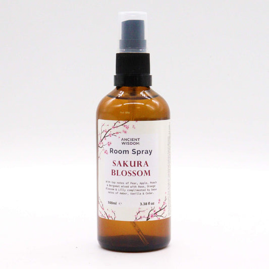 A brown glass bottle of room spray sits on a white background. The spray bottle is labeled “Sakura Blossom” and lists its scent notes.