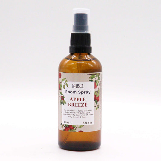 A brown glass bottle containing room spray sits on a white background. The label reads "ANCIENT WISDOM Room Spray APPLE BREEZE," describing its scent profile. The bottle is 100ml (3.38 fl oz).