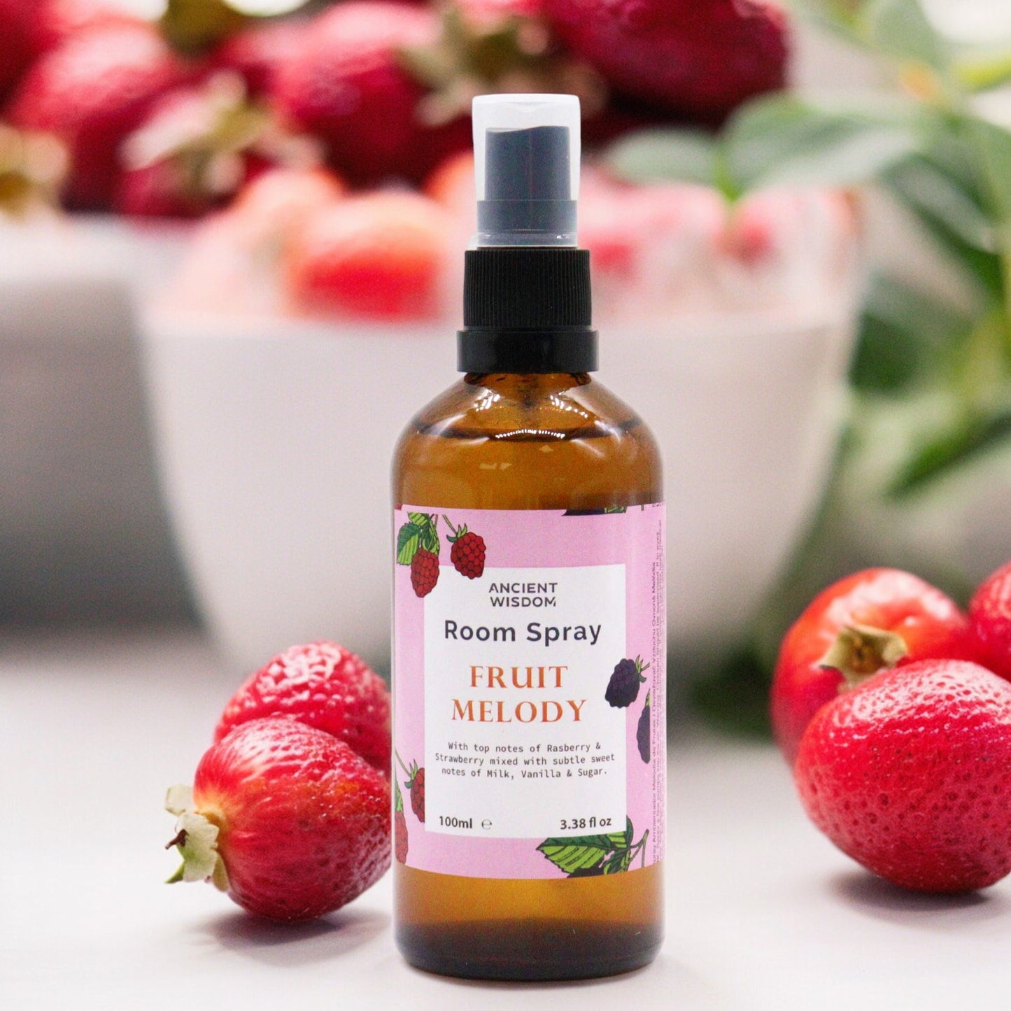 A brown glass bottle of room spray sits amidst fresh strawberries. The bottle is labeled “ANCIENT WISDOM Room Spray FRUIT MELODY,” describing its scent as raspberry, strawberry, milk, vanilla, and sugar.