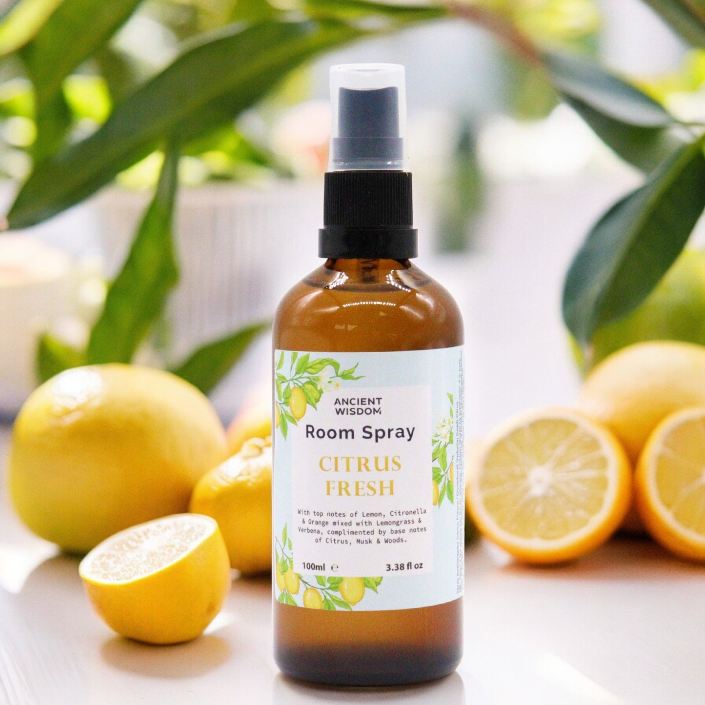 A brown glass bottle of "Ancient Wisdom Citrus Fresh" room spray sits among lemons. The bottle is a spray bottle, and the label indicates that it is 100ml (3.38 fl oz).
