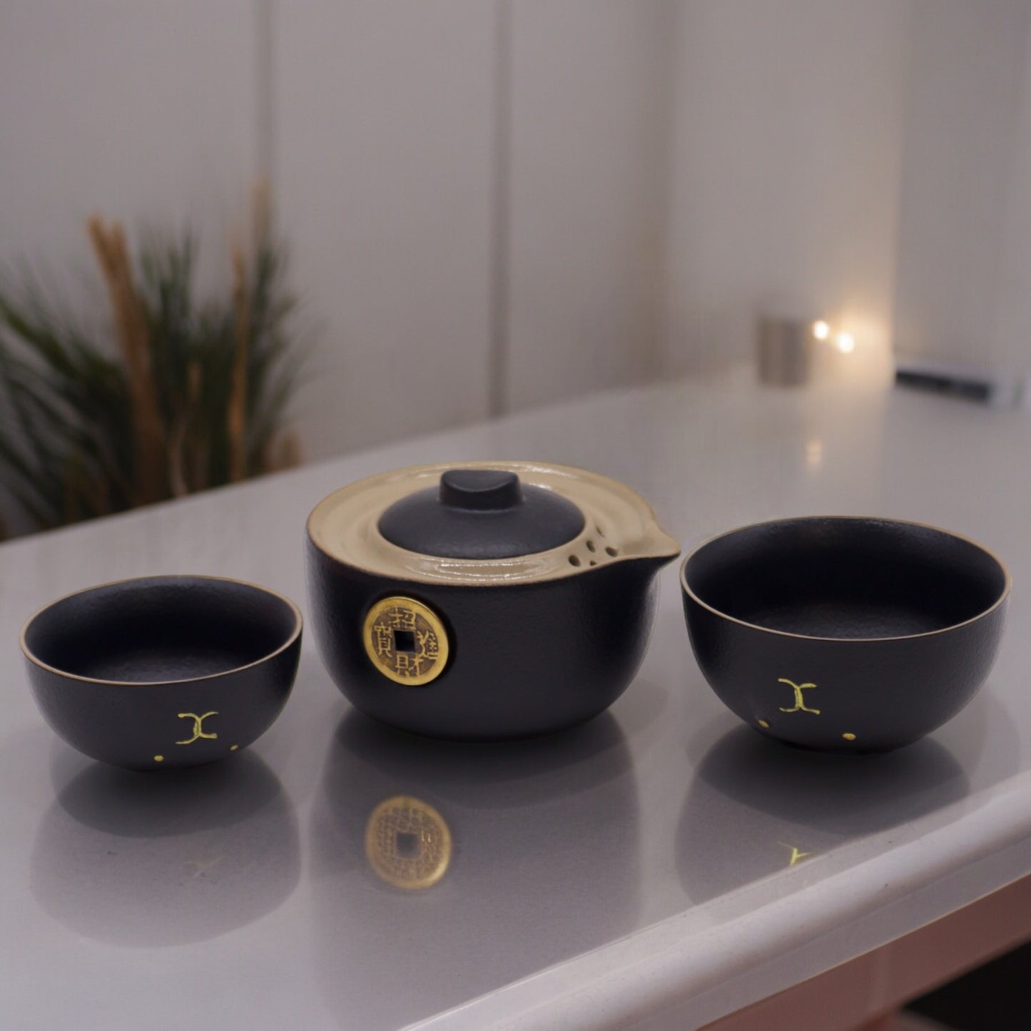A dark-grey ceramic teapot and two matching cups sit on a light-grey table. They appear unused, in a calm, well-lit room.