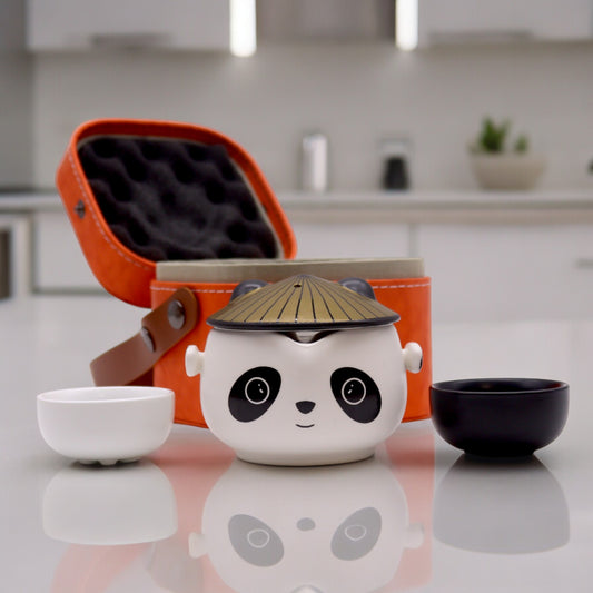 A panda-shaped tea set sits on a kitchen counter, nestled within an orange carrying case; two small bowls flank the set.