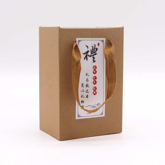 A brown cardboard box with gold ribbon handles sits on a white background. A label displays Chinese characters: 禮為緣之禮相逢. A red seal is also visible on the label.