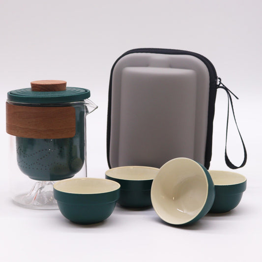A teal glass teapot with a wooden lid and infuser sits with four matching teal cups and a gray carrying case on a white surface.