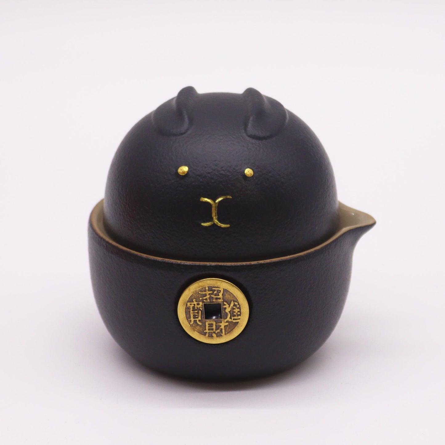 A black ceramic tea infuser, shaped like a rabbit, sits on a white background. The infuser has a small gold coin affixed to its base with Chinese characters.