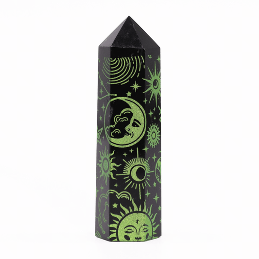 A black obelisk is decorated with green celestial designs, including a crescent moon, sun, and stars, standing upright on a plain white background.