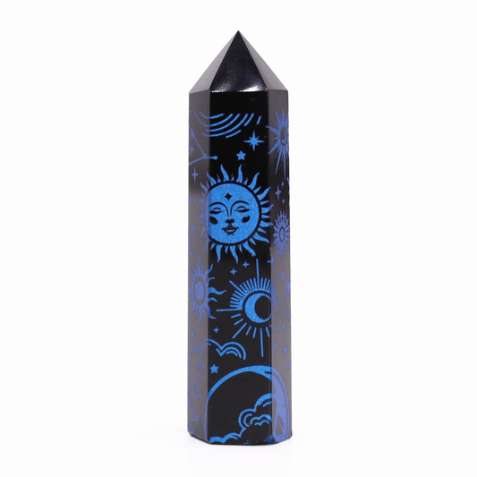 A black obelisk-shaped stone features blue cosmic designs including a sun, moon, and stars, positioned upright on a plain, white background.