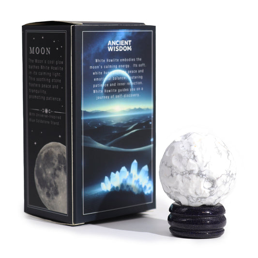 A white howlite sphere rests on a dark blue stand. It sits next to its packaging, which describes the stone's purported calming properties.
