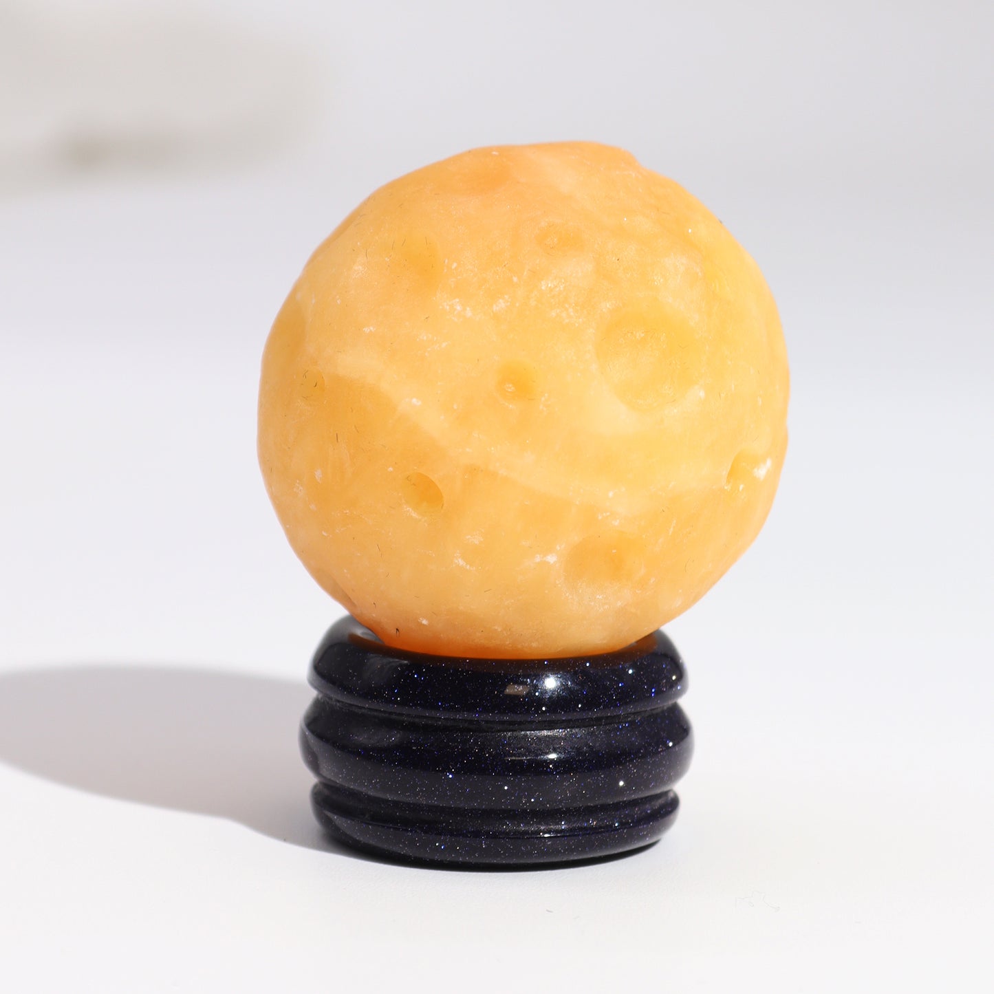 A yellow sphere, resembling a moon, rests on a dark blue, multi-layered stand. The scene is brightly lit against a white background.