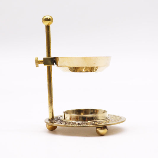 A brass incense burner, sits on a white surface.  The burner consists of a small bowl held aloft by a vertical rod and circular base.