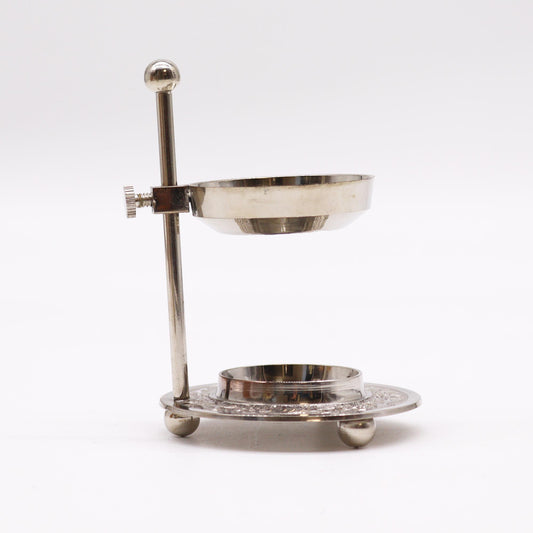A metallic stand holds a small bowl, elevated on a wider base with decorative detailing; it sits on a plain white surface.