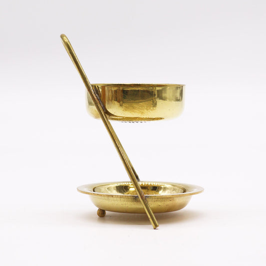 A brass tea infuser sits on a matching base; a single rod supports the infuser above the base.  The setup rests on a white surface.