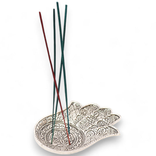 Intricately carved hand-shaped incense holder supports several thin, upright, red and green incense sticks. The patterns feature floral designs. The background is plain and white.