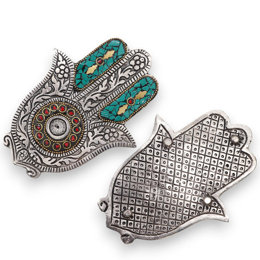Silver hamsa pendants; one features turquoise and red stone inlays with intricate floral engravings, while the other displays a grid pattern with raised dots, set against a plain backdrop.