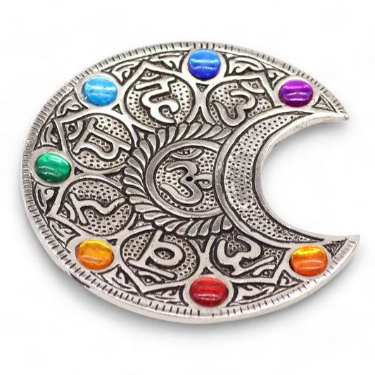 A decorative silver medallion features a stylized moon design with intricate patterns and colorful stones embedded around the edge. It rests on a white surface.
