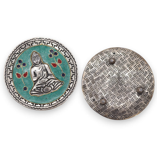 A round pendant features a silver Buddha seated against a turquoise background with red and blue floral accents, framed by geometric patterns. The reverse side shows a textured, grid-like design.