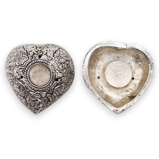 Two heart-shaped metal containers, one open revealing a hollow interior, the other closed with intricate floral engravings, placed on a plain white background.