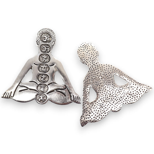 Metal figures depict a person meditating in a seated position. The front figure displays five circular symbols down the torso, while the back figure has a dotted texture.