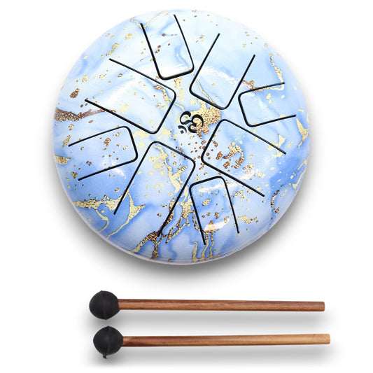 A blue and gold tongue drum with black cut-out shapes lies on a white surface. Two wooden mallets with black rubber tips are positioned below it.