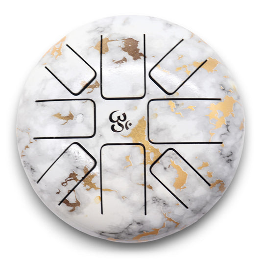 A round steel tongue drum features intricate golden and black patterns on a marbled white surface. Central cutouts create musical tongues, surrounding a small logo resembling stylized letters.