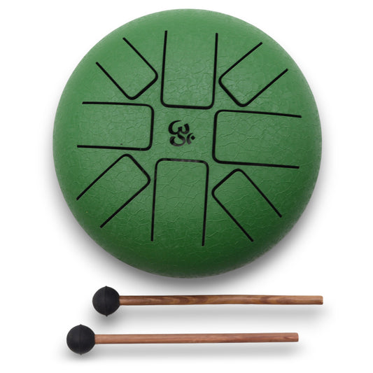 Green tongue drum with an Om symbol, featuring cut-out sections for different notes. Two wooden mallets with black rubber ends lie beneath it, all on a white background.