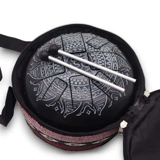 A tongue drum adorned with intricate patterns rests inside an open fabric case. Two mallets are positioned on the drum, indicating readiness for play. The case is partially visible.