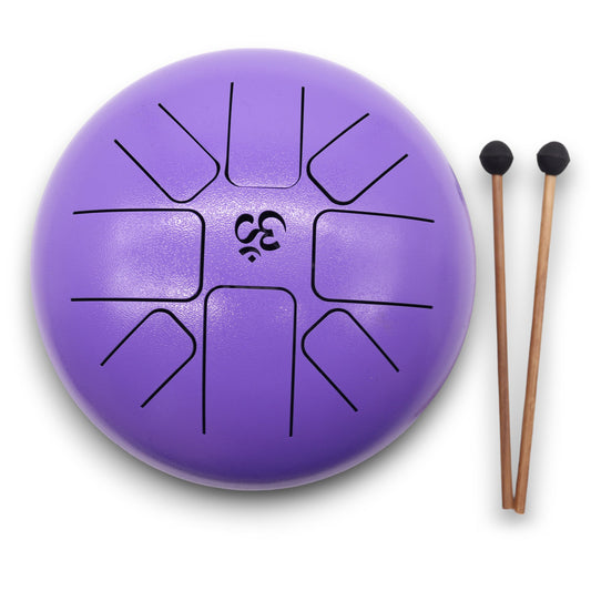 A purple tongue drum with black cut-out shapes, accompanied by two wooden mallets with black rubber tips, lies on a white surface.
