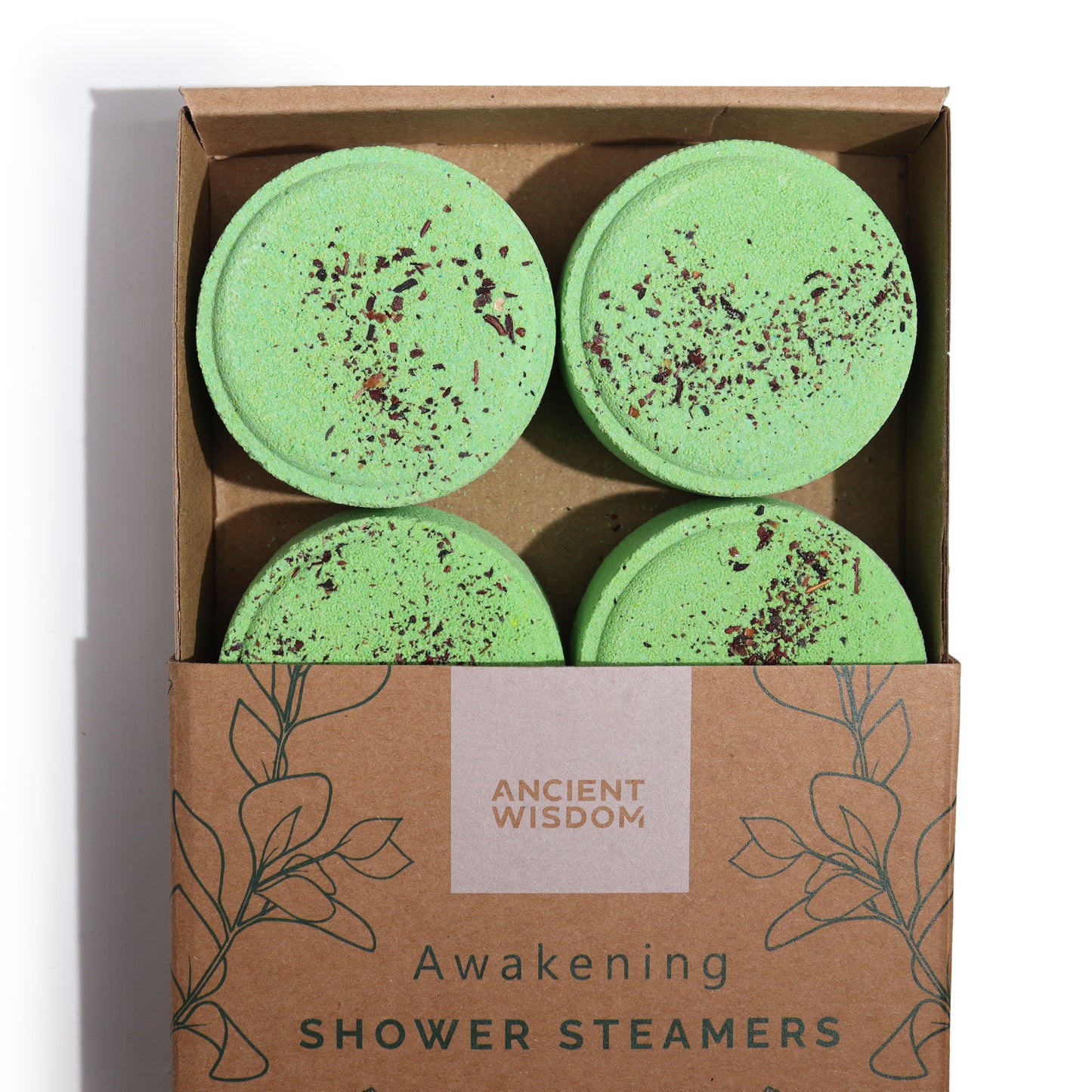 Four green shower steamers with sprinkled herbs rest in an open cardboard box labeled "Ancient Wisdom Awakening Shower Steamers," decorated with minimalist leaf illustrations.