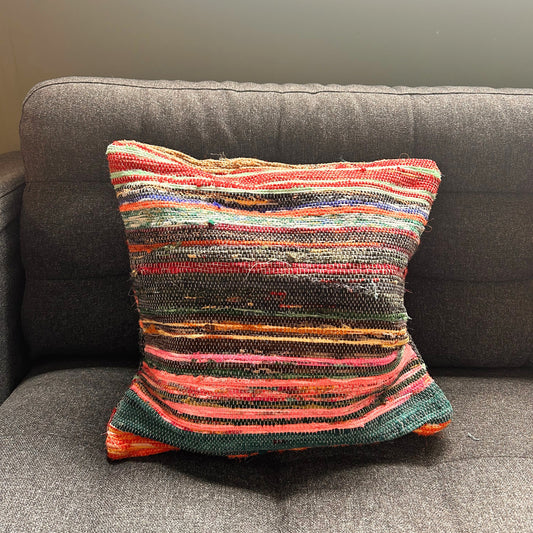 A colorful, striped woven pillow rests on a dark gray sofa, creating a contrast in a softly lit room.