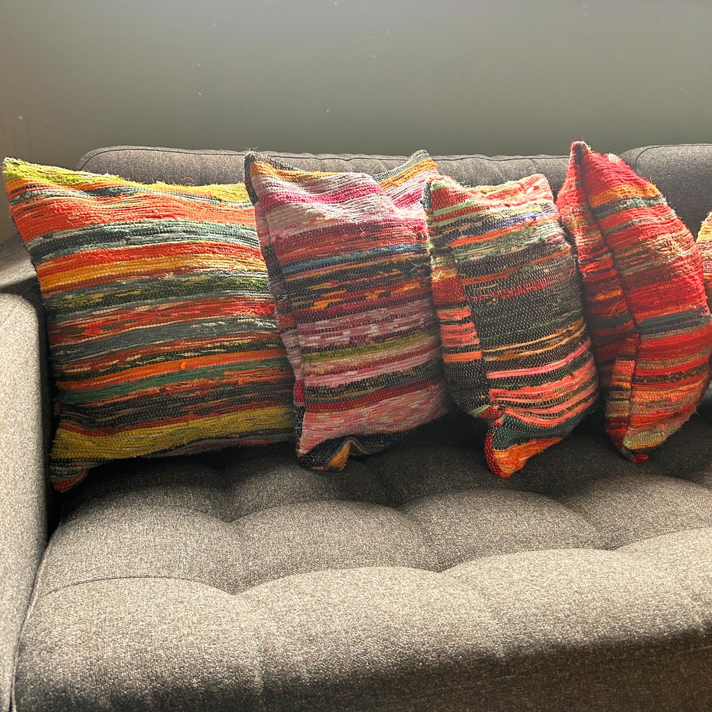 Striped multicolored pillows rest on a dark, tufted sofa in a well-lit room, creating a vibrant and cozy atmosphere.