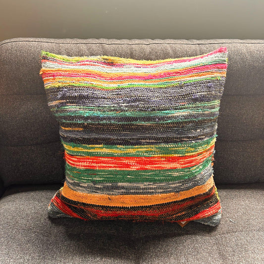 A colorful striped pillow rests on a dark gray sofa, featuring woven textures in vibrant hues like green, red, orange, and blue, creating a cozy and inviting atmosphere.