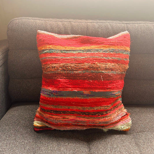 A colorful, striped woven cushion rests on a grey fabric sofa, illuminated by soft, natural light from above.