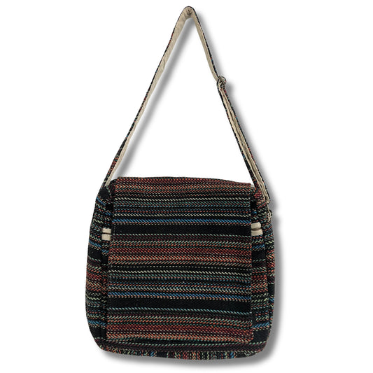 A multicolored woven shoulder bag with a flap closure hangs from a single strap. The bag features horizontal stripes in various colors, set against a plain white background.