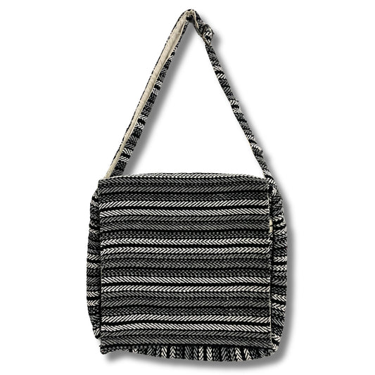 A black and white striped bag with a flap, featuring a long strap for carrying. The pattern resembles herringbone, creating a textured appearance against a plain white background.