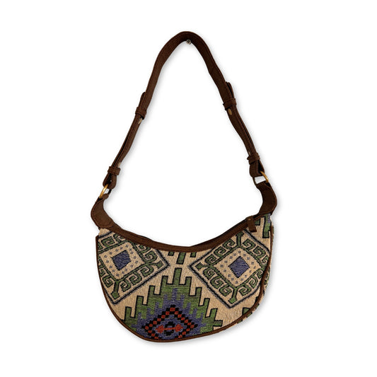 A fabric shoulder bag features an intricate geometric pattern in green, blue, and red. It has a brown adjustable strap and appears on a plain white background.