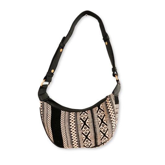 A patterned shoulder bag hangs by its black strap. The bag features intricate geometric designs in black and cream colors, set against a plain white background.