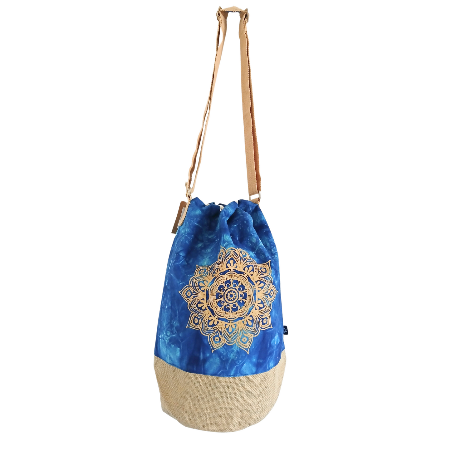A blue drawstring bag with a golden mandala design and a light brown bottom stands upright. It has a brown adjustable shoulder strap, set against a plain white background.