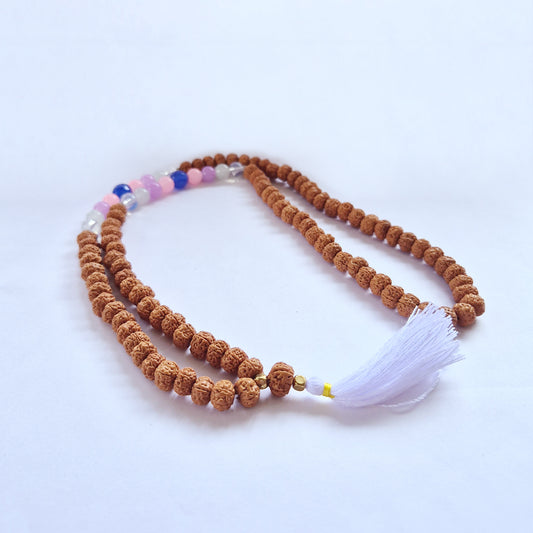 A mala necklace with brown beads, accented by a section of pink and blue beads, lies on a white surface, ending in a white tassel.