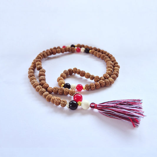 Brown prayer beads with small red, black, and white beads interspersed, ending in a multicolored tassel, lie coiled on a plain white background.