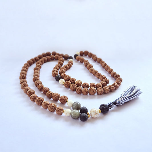 Beaded necklace with brown textured beads, interspersed with black and white stones, and finished with a gray tassel. It is laid out on a plain, light surface.