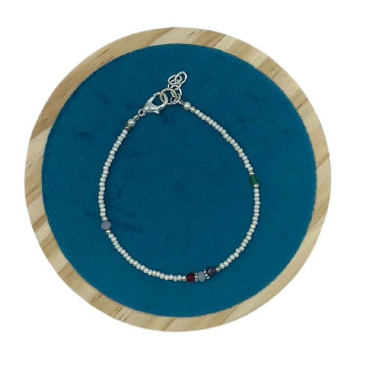 A delicate beaded bracelet with multicolored stones and a silver clasp rests on a circular blue velvet background, framed by light wood.