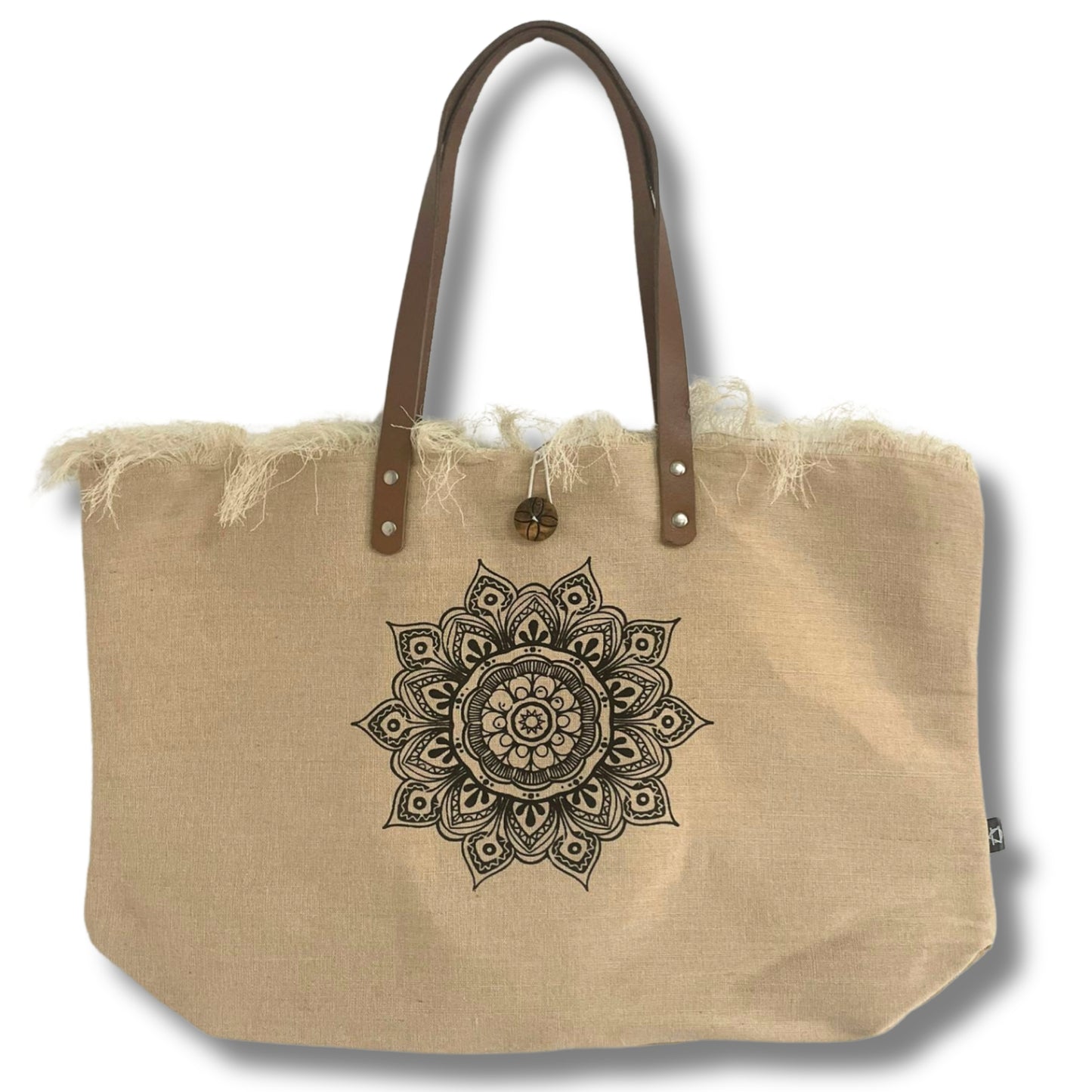 A beige tote bag features a black intricate mandala design at the center. It has frayed edges and brown leather handles, set against a plain white background.