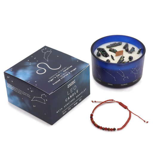 A blue candle with embedded stones sits next to a box labeled "LEO CANDLE WITH GEMSTONE BRACELET," featuring zodiac signs. Below is a red bracelet. Box text: "Tiger's Eye & Hematite, Frosted Citrus & Ginger, JUL. 23 - AUG. 22."