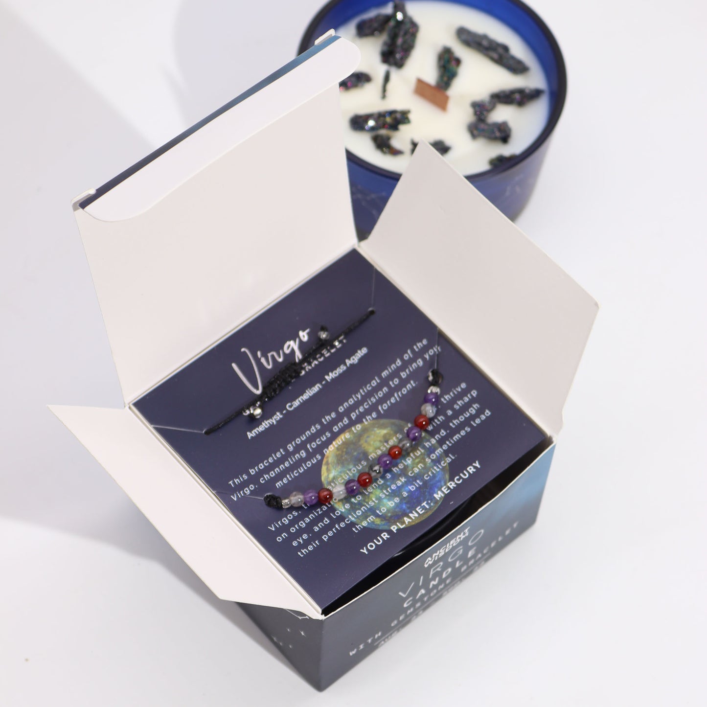 Box contains a Virgo-themed bracelet with amethyst, carnelian, and moss agate on a card. Text: "Virgo...YOUR PLANET: MERCURY." Nearby is a candle with dark crystals embedded in the wax.
